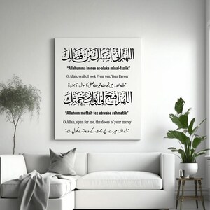 Könnte beinhalten: Ein weißer Leinwandkunstdruck mit schwarzer arabischer Kalligraphie und englischen Übersetzungen. Das Kunstwerk zeigt zwei Gebete, die über einem weißen Sofa mit einem grauen Überwurf und Kissen angezeigt werden. Ein kleiner Beistelltisch aus Holz trägt eine Topfpflanze.
