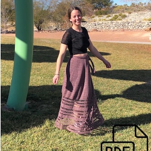 May include: A woman wearing a black top and a long, crocheted, mauve wrap skirt. The skirt has a lacy pattern and is tied at the waist. The woman is standing in a grassy area with a green structure in the background. The text "PDF" is visible in the lower right corner of the image.