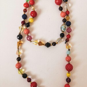 Puede incluir: Un collar de cuentas colorido con una variedad de formas y tama&ntilde;os. El collar presenta cuentas rojas, amarillas, azules, verdes y rosas, intercaladas con espaciadores dorados. Las cuentas est&aacute;n dispuestas en un dise&ntilde;o largo y fluido.