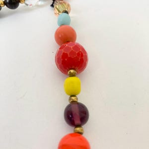 Puede incluir: Un collar de cuentas de colores con una variedad de cuentas redondas y facetadas en tonos de rojo, naranja, amarillo, morado y azul. Las cuentas est&aacute;n ensartadas con detalles met&aacute;licos dorados, creando un accesorio vibrante.