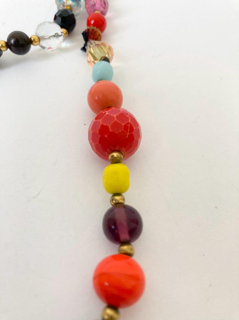 Puede incluir: Un collar de cuentas de colores con una variedad de cuentas redondas y facetadas en tonos de rojo, naranja, amarillo, morado y azul. Las cuentas est&aacute;n ensartadas con detalles met&aacute;licos dorados, creando un accesorio vibrante.