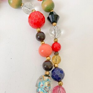 Puede incluir: Un collar de cuentas de colores con una variedad de formas y tama&ntilde;os. Las cuentas son en tonos de rojo, rosa, naranja, verde, negro, azul y transparente. Espaciadores dorados separan las cuentas. El collar est&aacute; sobre un fondo blanco.