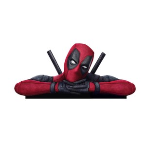 May include: A Deadpool character cutout featuring a red and black suit with a mask, white eye patches, and black gloves. The figure is shown from the chest up with arms crossed, resting on a flat edge, with two sword hilts visible behind the shoulders.