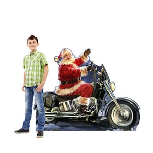 May include: A cardboard cutout of Santa Claus riding a black motorcycle. Santa is wearing a red suit with white fur trim and a matching hat. The motorcycle has chrome details and a large front tire. A young person is standing next to the cutout.