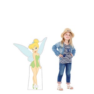 May include: A cardboard cutout of Tinkerbell in a green dress with light blue wings stands next to a young girl. The girl wears a straw hat, a denim jacket, a striped shirt, blue jeans, and sandals.