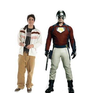 May include: A life-size cardboard cutout of a person in a Peacemaker costume, with a red and blue jacket, white pants, and a silver helmet. Next to it is a person wearing a white jacket with red stripes, a black t-shirt, and brown pants.