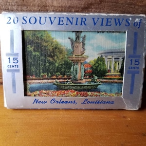 以下が含まれることがあります： ルイジアナ州ニューオーリンズの記念品風景20枚がセットになったヴィンテージのポストカード。ポストカードには、像のある噴水と花が咲く池が描かれています。ポストカードのテキストには、「20 Souvenir Views of New Orleans, La. 15 Cents」と記載されています。