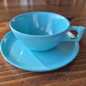 May include: A light blue ceramic teacup and saucer set. The cup has a rounded shape and a handle. The saucer is a simple round shape.