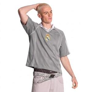 May include: A gray short-sleeved soccer jersey with white accents and a team emblem on the chest. The jersey has a white collar and white stripes on the sleeves. The person is wearing a silver chain necklace and a zebra-print belt.