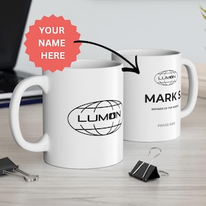 May include: Two white ceramic mugs with black logos and text. One mug displays the word "LUMON" inside an oval with a globe design. The other mug has the name "MARKS", the text "REFINER OF THE MONTH", and "PRAISE KIER".