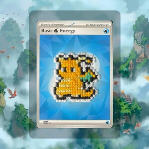 May include: A rectangular trading card featuring a blue background with a geometric pattern and the text Basic Energy. Centered on the card is a yellow and black pixelated creature figure created with textured embroidery or cross-stitch thread.