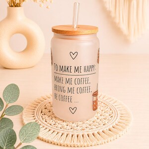 Könnte beinhalten: Ein Trinkglas aus Milchglas mit Bambusdeckel und einem Trinkhalm aus klarem Glas. Das Glas ist mit schwarzem Text bedruckt: TO MAKE ME HAPPY: MAKE ME COFFEE, BRING ME COFFEE, BE COFFEE... sowie kleinen Herzsymbolen und Kaffeetassen-Grafiken.