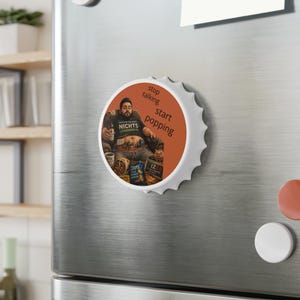 Könnte beinhalten: Ein runder Magnet mit weißem Rand und brauner Mitte. Der Magnet zeigt eine Illustration einer Person, die mit Essen und Getränken in einem Stuhl sitzt. Der Text auf dem Magneten lautet "stop talking start popping."