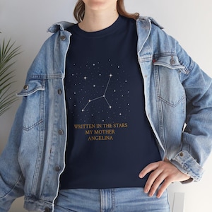 Könnte beinhalten: Marineblaues T-Shirt mit Sternbild-Design und dem goldenen Text "WRITTEN IN THE STARS MY MOTHER ANGELINA". Das T-Shirt hat einen Rundhalsausschnitt.