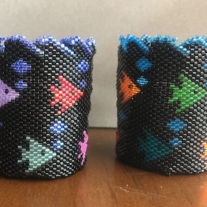 May include: Two small black beaded containers with colorful fish and star designs. The containers have a scalloped top edge.