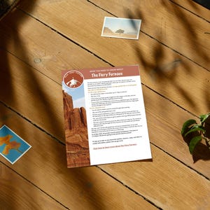 May include: A wooden surface with a brochure titled "The Fiery Furnace" featuring a desert landscape image. Two small photographs and a leafy green plant are also on the wood. The brochure has text and a logo.