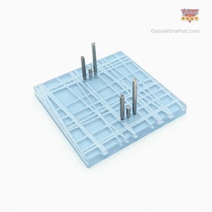 May include: A square, light blue glass art piece with a white grid pattern. Several silver metal rods of varying heights are embedded in the glass. The logo "Glass Past" and the website address "GlassWithaPast.com" are visible in the upper right corner.