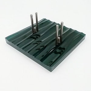 May include: A dark green glass sculpture with a wavy surface and four silver metal rods sticking up from the surface.