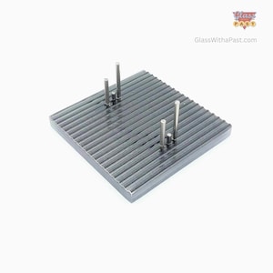 May include: A dark gray, square, ridged metal display stand with four silver metal posts of varying heights. The stand is designed to hold items. The website GlassWithaPast.com is visible in the upper right corner.