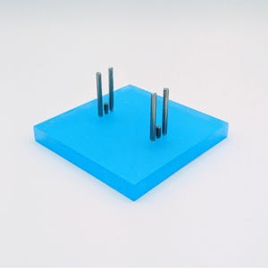 May include: Two sets of silver metal rods stand upright on a bright blue square base. The rods are arranged in a vertical line, with the tallest rod in the center.