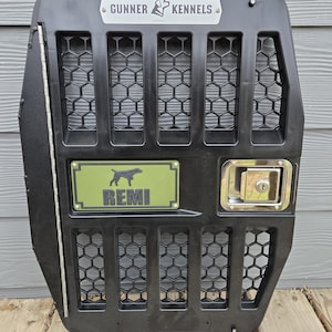 May include: Black dog kennel door with a metal latch and the text "GUNNER KENNELS" at the top. The door has a honeycomb pattern and a green nameplate that says "REMI" with a dog silhouette.