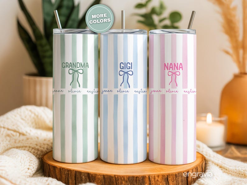 May include: Three personalized stainless steel tumblers with vertical stripes in pastel colors: green, blue, and pink. Each tumbler has a name: "Grandma," "Gigi," and "Nana," with a bow graphic and names below. The tumblers have a silver straw.