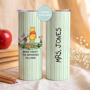 May include: A cylindrical stainless steel tumbler with a light green vertical striped pattern. One side features Winnie the Pooh and Piglet with the text 'NEVER FORGET THE DIFFERENCE YOU MAKE'. The other side displays the custom text 'MRS. JONES'.