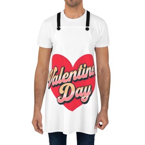 以下が含まれることがあります： 赤いハートに「Valentine Day」の文字が書かれた白いエプロン。文字は筆記体で、ピンクと黄色のグラデーションになっています。黒いストラップが付いています。