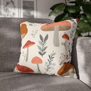 May include: A white throw pillow with a pattern of orange and red mushrooms and gray leaves on a white background.