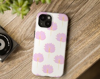 May include: A white phone case featuring a repeating pattern of pink floral designs with yellow stems. The phone case is on a wooden surface, with a camera and greenery in the background.