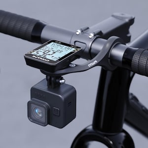 May include: Black bicycle handlebar with a mounted CYCLAMI cycling computer displaying data. A black action camera is mounted below the computer. The handlebar is black with black grips.