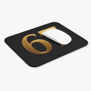 May include: Black rectangular mousepad with a gold number 6 and a gold rectangle. A white wireless mouse is on the mousepad. The number 6 is in a bold, serif font. The mousepad is a computer accessory.