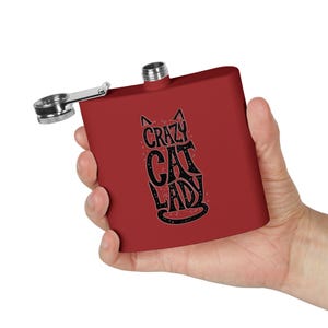 May include: Red metal flask with a black and white graphic of a cat and the text "Crazy Cat Lady".