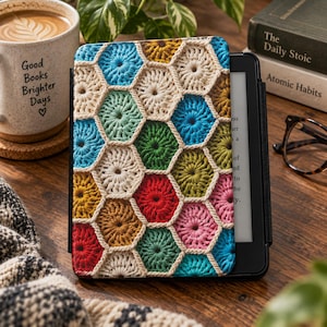 May include: A protective e-reader cover featuring a colorful crochet pattern of interconnected hexagons in shades of blue, green, red, pink, yellow, and brown, outlined in cream-colored yarn, attached to a black electronic reading device.