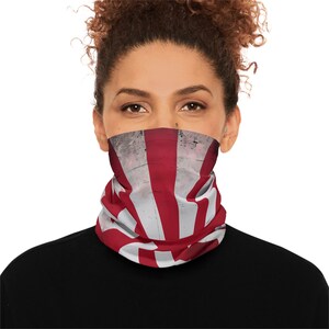 Könnte beinhalten: Ein rot-weiß gestreifter Gesichtsschutz mit Flaggenmuster wird um Hals und unteres Gesicht getragen. Der Stoff hat ein abgenutztes, Vintage-Aussehen. Die Person trägt ein schwarzes Oberteil.
