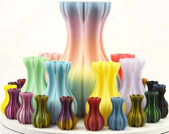 May include: A collection of colorful, 3D-printed vases in various sizes and shades, including blue, green, yellow, purple, and a large rainbow-colored vase. The vases have a unique, fluted design.