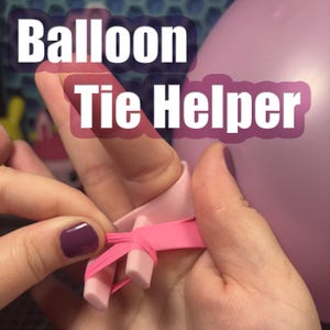 May include: A pink balloon tie helper is shown with the text "Balloon Tie Helper". The tool is being used to tie a pink balloon. The tool is pink and has a ring and two pegs.