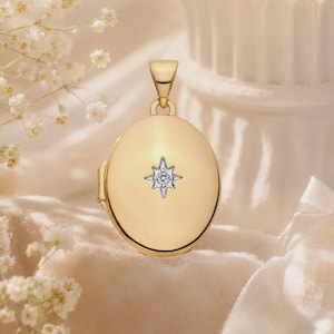 May include: An oval gold locket pendant featuring a polished finish and a central silver-toned star-shaped inlay with a small embedded clear stone. The locket has a simple bail at the top for attachment to a chain, showcasing a smooth, reflective surface.