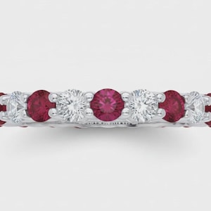 Puede incluir: Un anillo de banda plateada con un patrón alterno de rubíes rojos redondos y diamantes blancos transparentes en engaste de garras. El anillo muestra una fila continua de piedras preciosas en la parte frontal con acabado metálico.