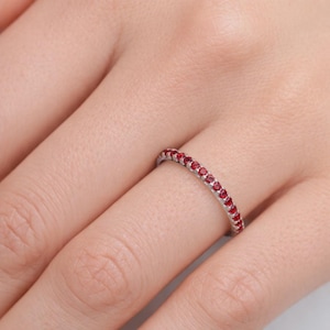 Pode incluir: Um anel fino de metal prateado com uma fila cont&iacute;nua de pequenas pedras redondas de um vermelho vibrante, cravadas ao longo de toda a circunfer&ecirc;ncia. O anel &eacute; usado num dedo, destacando a disposi&ccedil;&atilde;o uniforme das pedras vermelhas no metal.