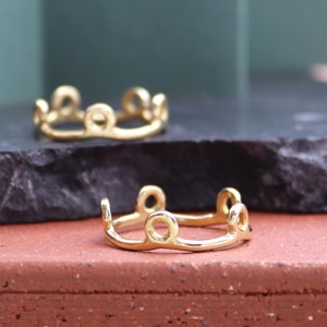 Könnte beinhalten: Zwei goldene Ringe mit einem einzigartigen Design, das aus einer Reihe verbundener Kreise besteht. Die Ringe werden auf einer schwarzen und braunen Oberfläche präsentiert.