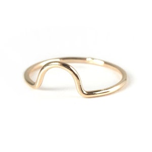 May include: A gold-toned ring with a curved, arch-shaped design. The ring is simple and minimalist.