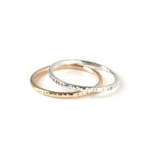 May include: Two thin, textured rings, one silver and one gold, stacked on top of each other.