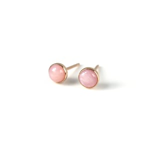 May include: A pair of small, round pink opal stud earrings with gold settings.