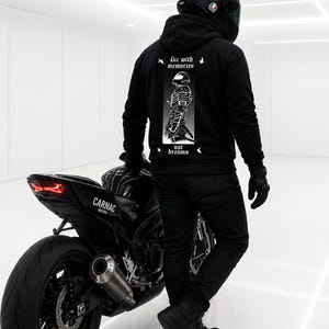 May include: A black hooded sweatshirt featuring a white graphic on the back of a samurai figure with the text Die with memories not dreams. The hoodie is worn with black jeans, black boots, black gloves, and a black motorcycle helmet.