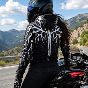Può includere: Una felpa nera con cappuccio caratterizzata da un motivo grafico a fulmini bianchi sul retro e sulle maniche. La felpa è indossata con jeans neri, guanti da moto neri e un casco integrale nero, mentre si è in sella a una motocicletta.