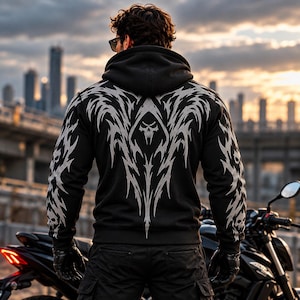 May include: A black hooded sweatshirt featuring a large, light gray tribal-style graphic on the back. The design incorporates a central skull motif with sharp, angular patterns extending across the shoulders and down the sleeves to the cuffs.