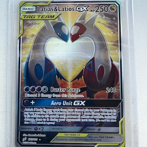 Puede incluir: Una carta coleccionable de Pokémon con Latias & Latios GX, un Tag Team. La carta tiene un fondo dorado y blanco con dos criaturas estilizadas en azul y rojo. El texto incluye "Buster Purge" y "Aero Unit GX". La carta está en una funda protectora.