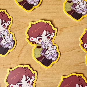 May include: A set of six stickers featuring a cartoon character with brown hair holding a white fluffy creature. The stickers are on a wooden surface.