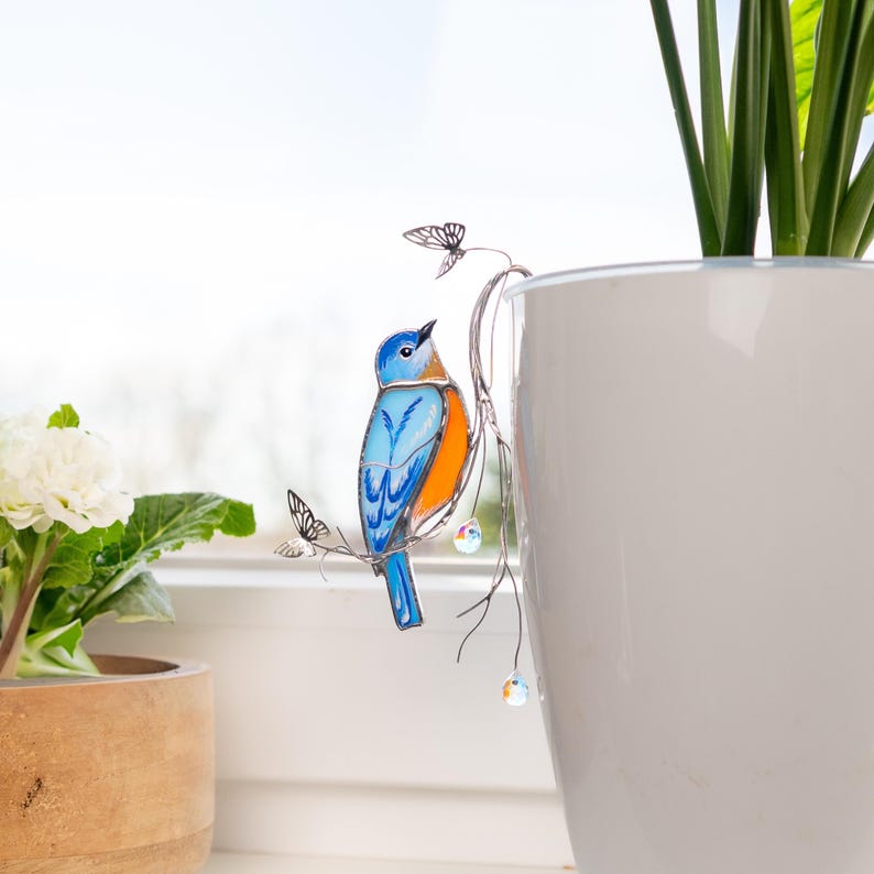 Artistic stained glass bluebird with crystal details and butterfly charm – a unique decor piece.